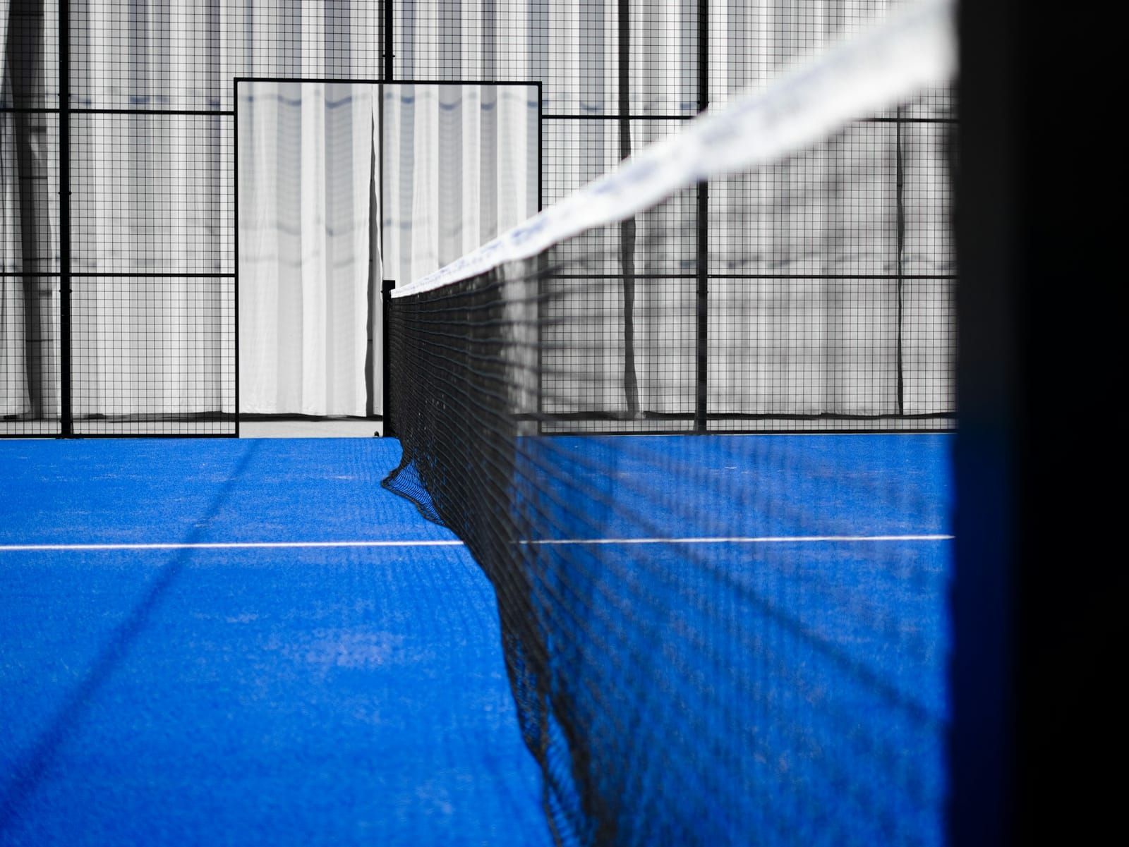 Filet d’un terrain de padel bleu entouré de vitrages