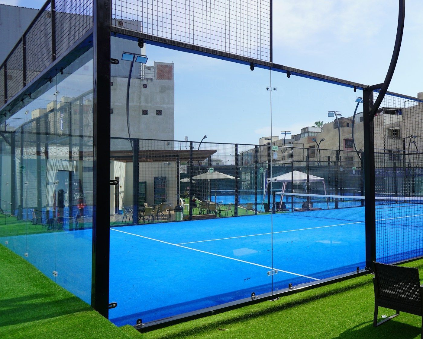 Terrain de padel panoramique aux vitrages transparents, gazon synthétique autour