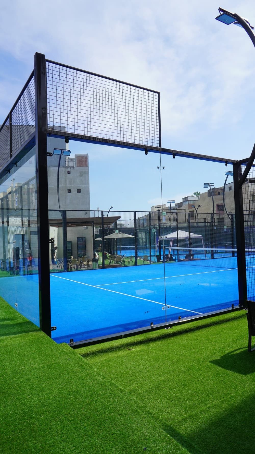 Terrain de padel panoramique aux vitrages transparents, gazon synthétique autour