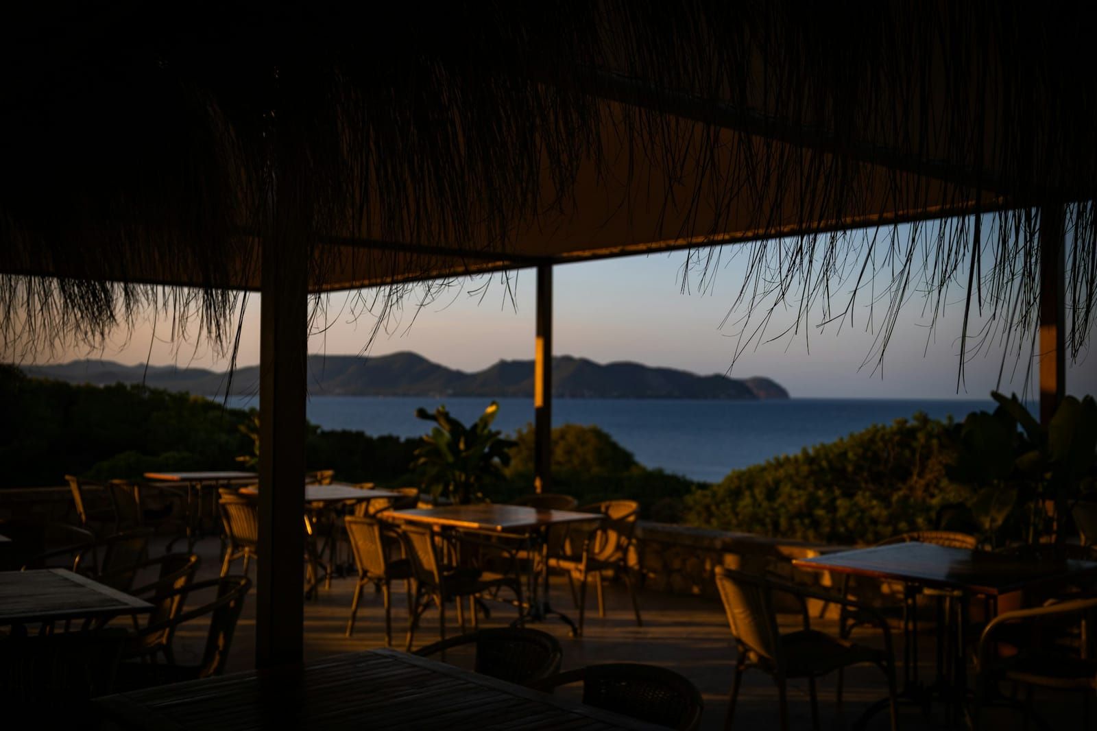 Terrasse ombragée avec tables et vue sur la mer au coucher du soleil